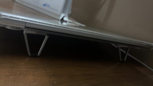 Close-up of a customer's Casence AirStand elevating a silver laptop from a dark wooden surface.