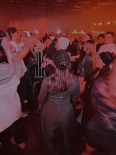 Partial view: Reviewer from behind wearing dark baggy pants in a crowded, dimly-lit room.