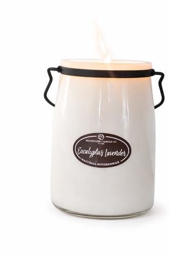 Customer's lit candle in a white, milk-jug-style jar with black handles and a visible flame.