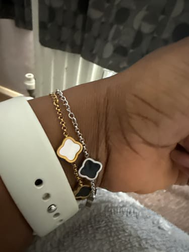 Customer wears two stacked Celine Clover Bracelets on their wrist, one gold with white clovers and one silver with black clovers.