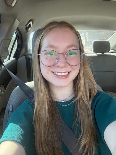 Reviewer smiling while wearing a delicate silver necklace from the Valentines Bundle in a car.