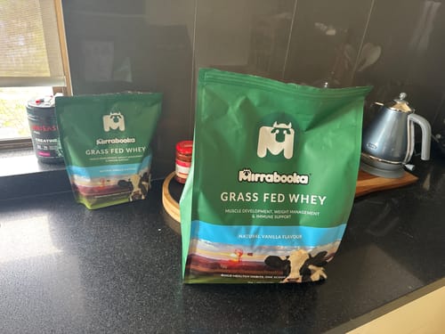 Customer's two green bags of Mirrabooka Grass Fed Whey, one large and one small, on a kitchen counter.