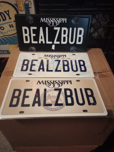 Reviewer shows three custom Mississippi metal license plates, all with 'BEALZBUB' in black, white, and beige styles.