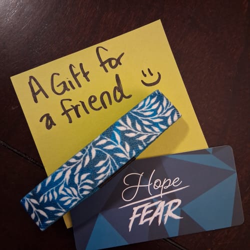 Customer's blue Hope Over Fear Bracelet with a vine pattern, shown with a gift note and the product packaging.