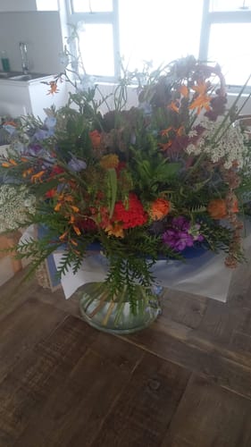 Customer's large, colorful Wild and Free Bouquet displayed in a glass vase on a wooden surface.
