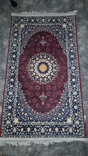 Reviewer's Moroccan Padded Prayer Mat with an intricate burgundy and blue design laid flat on a rug.