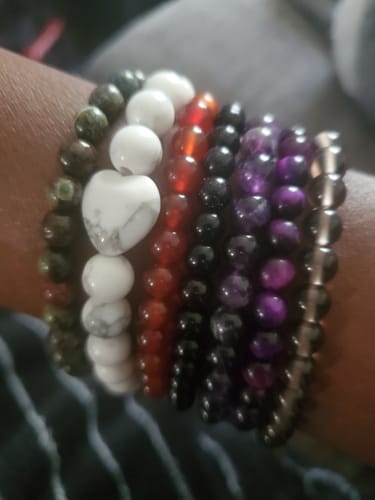Close-up of a customer's wrist wearing a stack of colorful crystal bracelets, including a white howlite one with a heart bead.