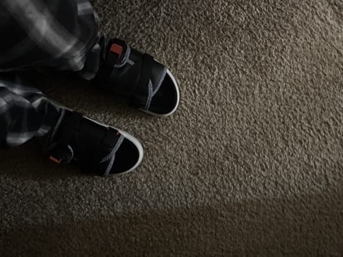 Customer wearing a pair of black Mystery DracoSlides with white-trimmed soles on a carpet.