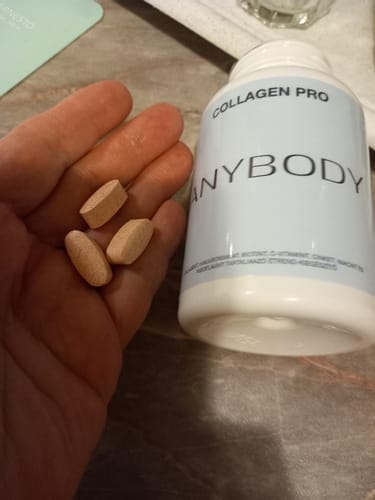 Vásárló kezében tart három Anybody Collagen Pro kapszulát a termék fehér flakonja mellett.