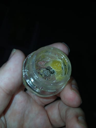 Close-up of a customer's hand holding a nearly empty glass jar of Live Resin THCa Diamonds.
