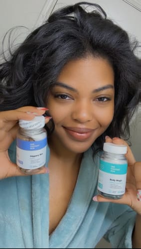 Reviewer smiling while holding a bottle of Body Magic Chlorophyll Pills and another product from the brand.
