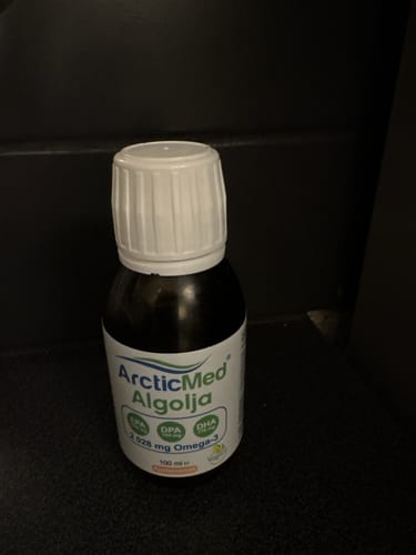 Kundens flaska med ArcticMed Algolja står på en mörk yta.
