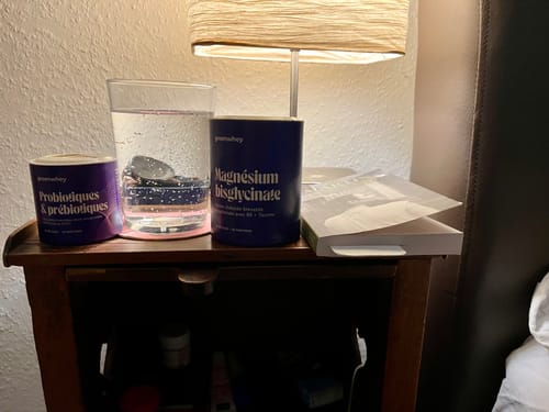 Le pot de Magnésium Bisglycinate d'un client posé sur une table de chevet à côté d'une lampe.