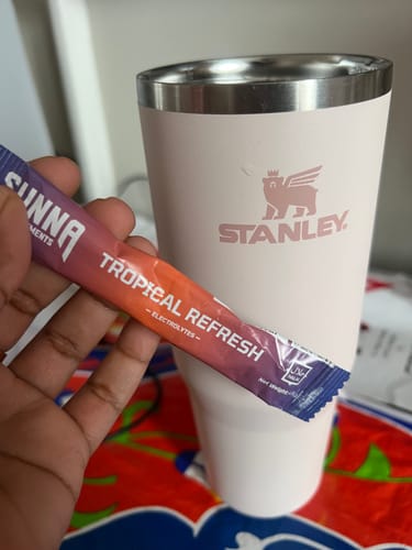 Customer holding a sachet of Tropical Refresh Electrolytes in front of a light pink tumbler.