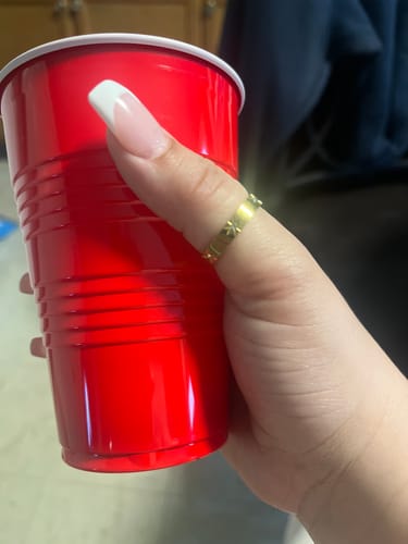 Customer holding a red cup, showing the gold North Star Ring worn on their thumb.