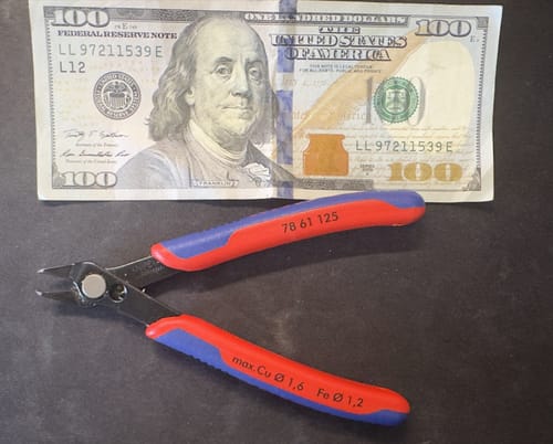 Reviewer's Knipex Electronics Super Knips pliers with red and blue handles, shown next to a 100 dollar bill for scale.