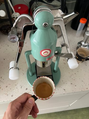 Reviewer holding a small, decorated cup with a fresh espresso shot of Coconut Float coffee.