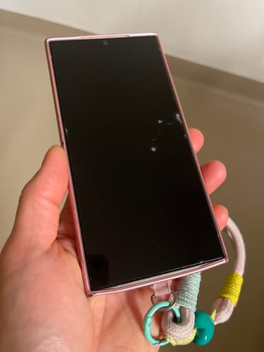 Ein Rezensent hält ein Smartphone in der Hand, das eine beschädigte Schutzfolie zeigt, die den Bildschirm geschützt hat.