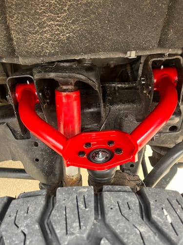 Customer's custom powder-coated red Upper Control Arms installed on a truck, seen from below looking up at the suspension.