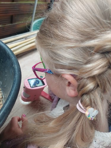 Rezensent zeigt ein Kind, das das rosa Edubini Abenteuer-Mikroskop benutzt.