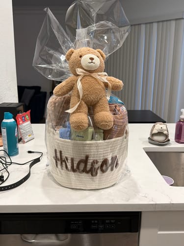 Reviewer's Animal Plushie Toy, a light brown teddy bear, sitting atop a personalized white gift basket wrapped in cellophane.