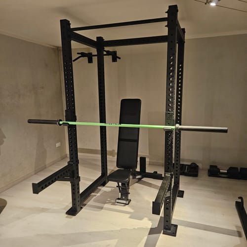 Das schwarze R8-Base 1 Power Rack eines Kunden, aufgebaut in einem Raum mit einer Hantelbank und einer Langhantel.