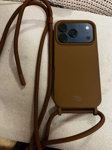Cliente mostrando a Case Mocha Mousse na cor marrom com uma alça, em um celular.