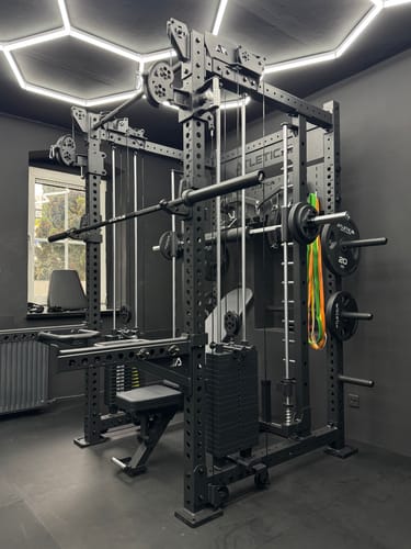 Kundenfoto des komplett montierten R8 Bradley Power Racks in einem dunklen, modernen Homegym.