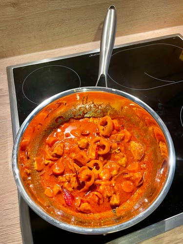 Rezensent kocht ein Hähnchen-Curry in der gehämmerte Titan-Wokpfanne auf einem Kochfeld.