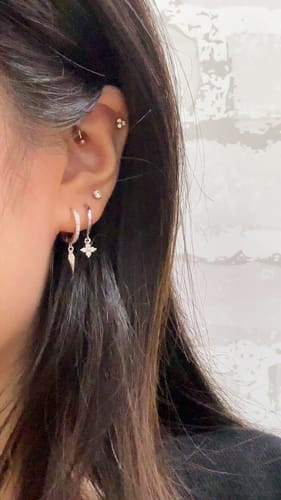 Reviewer's ear showing the Lucky Charm White/Silver huggie with a crystal clover charm, worn with other earrings.