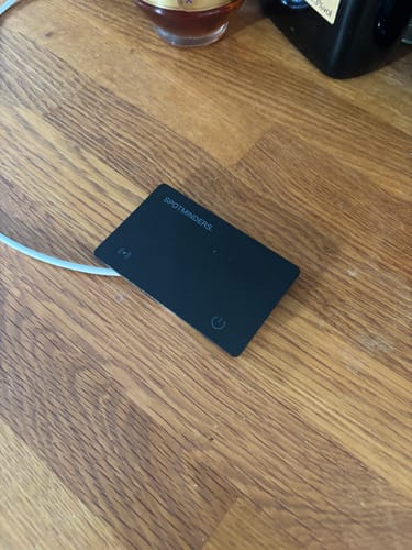 Customer's black SPOTMINDERS wireless charger plugged in and sitting on a wooden surface.