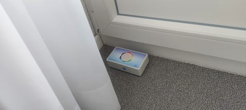 Der weiße HAMONI® Harmoniser eines Kunden, platziert auf dem Teppichboden in einer Ecke.