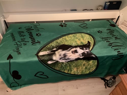 Ein Kunde zeigt seine grüne personalisierte Decke 'Meine Lieblinge' mit einem Hundefoto auf einem Bett.