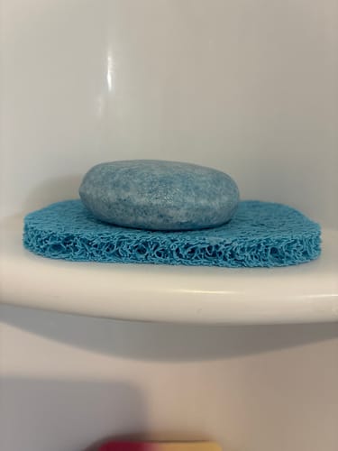 Customer's light blue Seaside Luxe Shampoo Bar on a porous blue soap dish on a shower shelf.