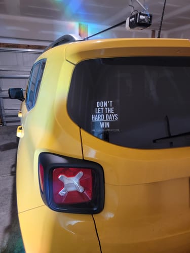 Reviewer's white Hard Days decal applied to the back window of a yellow car in a garage.