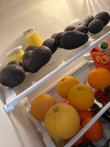 Ein Kunde zeigt die vielen dunklen Mini-Hass-Avocados auf einem Regal in seinem Kühlschrank.