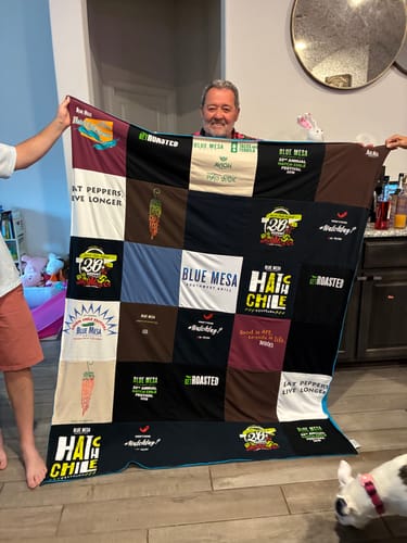 Customer holding up a large, multicolored Project Repat T-Shirt Quilt with another person in a living room.