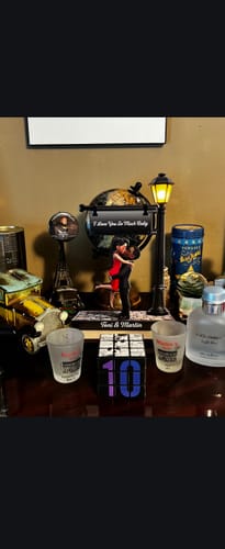 Customer's personalized wooden plaque of a couple under a lamppost, displayed on a dark table among other mementos.