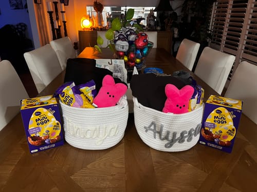 Customer's two personalized knitted baskets with names, filled with Easter candy and toys on a dining table.