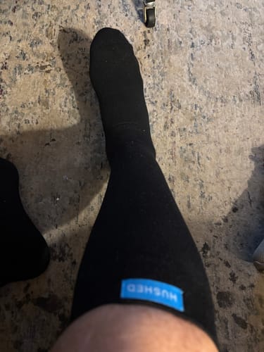 Reviewer's leg wearing a black Performance Eucalyptus Compression Sock, with the blue logo tag visible at the top.
