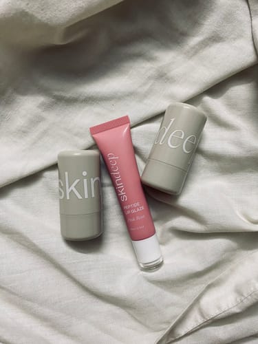 Customer's Lip Glaze+Velvet Flush Duo, including a pink lip glaze tube and two grey stick containers, on a white cloth.