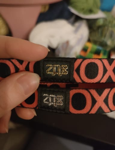 Close-up of a customer comparing two red F&F Colorwheel Bracelets, one with a gold tag and one with a silver tag.