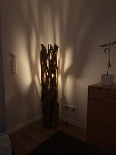 Die Teak-Wurzelholz-Stehlampe eines Kunden leuchtet in einer Zimmerecke und wirft stimmungsvolle Schatten an die Wand.