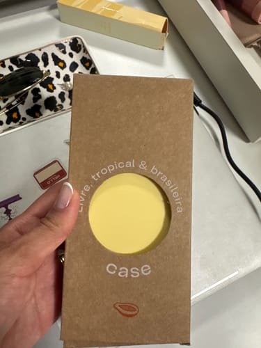 Cliente segurando a embalagem da case Nora, mostrando o produto amarelo pela abertura circular.