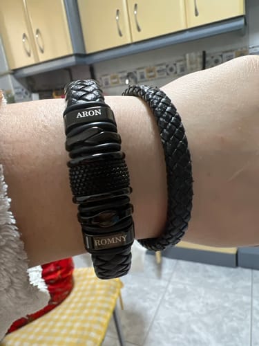 Customer's wrist wearing the personalized black multi-strand bracelet with the names 'Aron' and 'Romny' engraved.