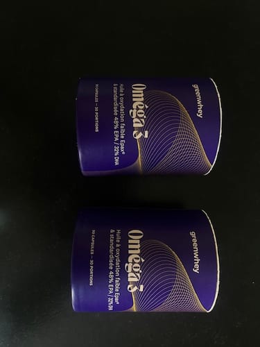 Client montrant deux pots violets du produit Oméga 3 EPAX® sur une surface sombre.