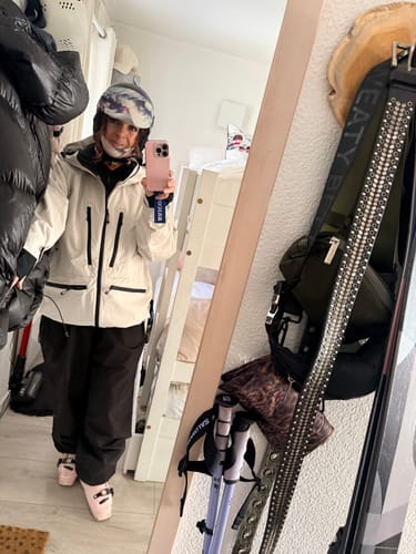 Reviewer takes a mirror selfie wearing the off-white snow jacket, helmet, and ski boots in a room.