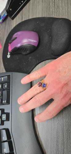Customer's hand wearing the Navae Birthstone Ring with a red pear-cut stone and a blue radiant-cut stone.