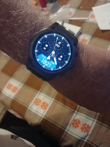 Reviewer's wrist showing a black smartwatch with an illuminated face displaying fitness data.