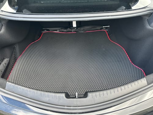 Recenzent pokazuje czarną, dopasowaną matę do bagażnika z czerwonym obszyciem, umieszczoną w bagażniku samochodu.